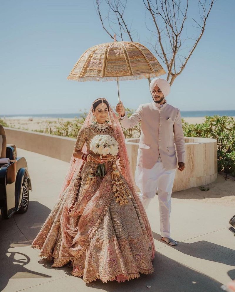 Bride entering under an umbrella that matches her lehenga