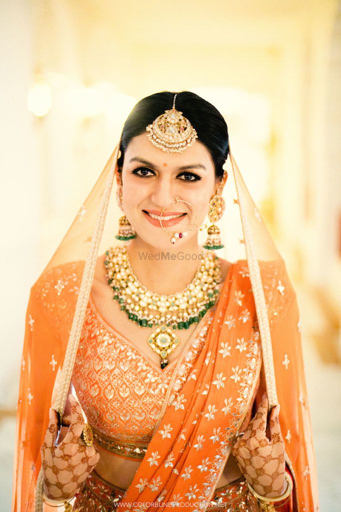 Photo of A bride in orange with gold and turquoise jewellery poses for the camera.