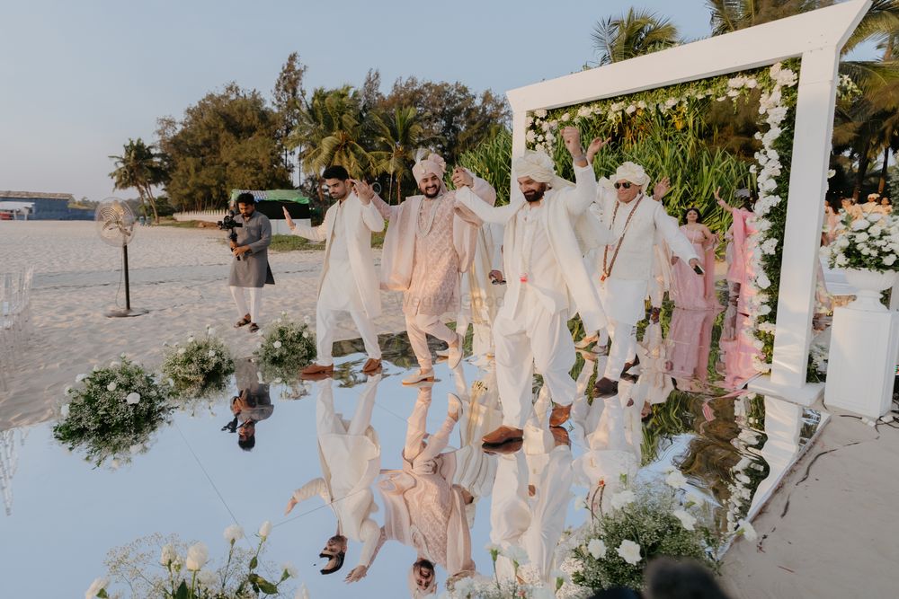 Photo of The groom entry with his groomsmen in all white on a mirror aisle as he walks down the mandap