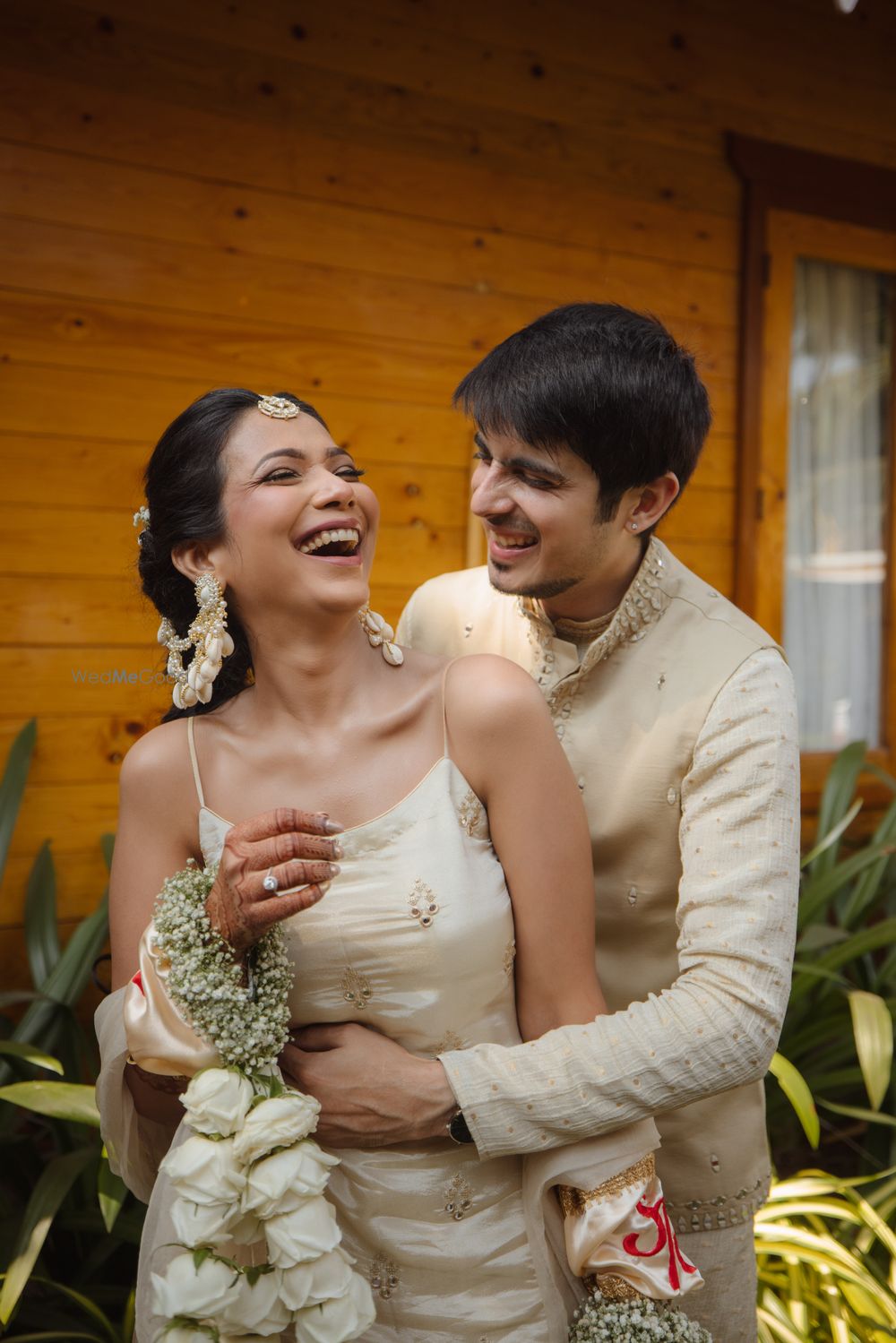 Photo of Fun haldi photo with the couple twinning in beige outfits and the bride in baby breath floral jewellery with seashells