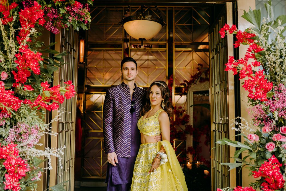 Photo of groom in purple indo western and bride in yellow lehenga for mehendi ceremony