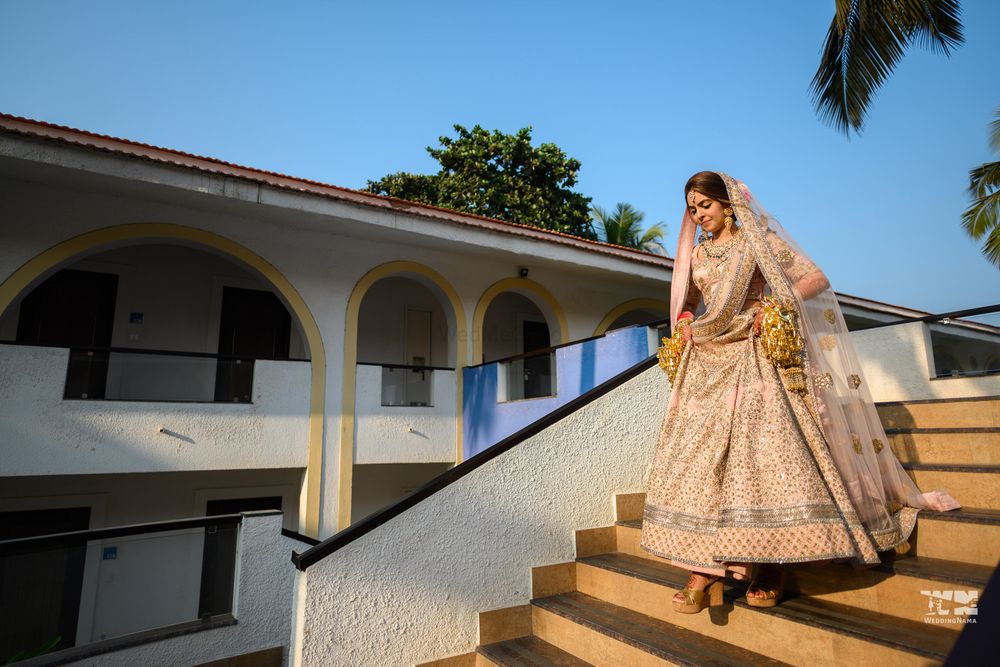 Photo of A bride walking down the stairs in a blush pink lehenga for her morning wedding