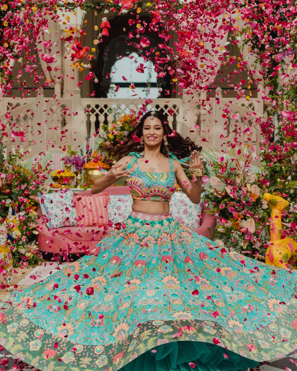 Photo of Fun bridal twirling shot in a turquoise blue floral lehenga with a flower shower on her mehendi