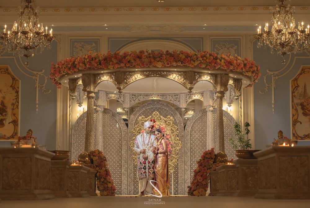 Photo of couple pose against grand south indian gold mandap