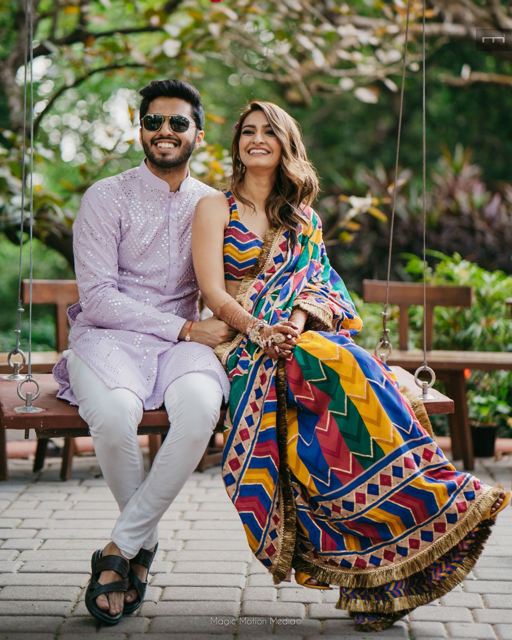 Photo of Adorable shot of the couple on a swing set with the bride in a multi-coloured saree and groom in a lilac kurta
