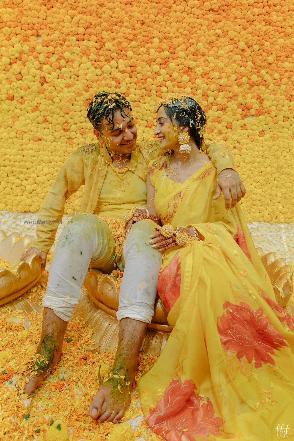 Photo of happy haldi couple shot against floral wall backdrop