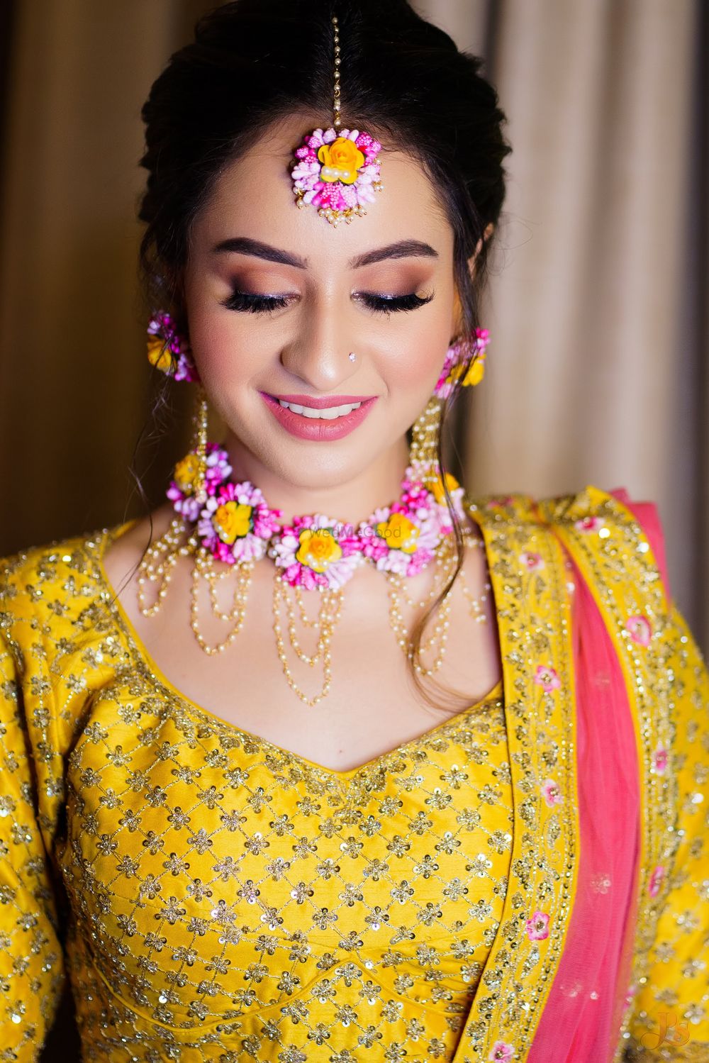 Photo of Bride wearing a yellow & pink lehenga with matching floral jewellery on her Mehendi