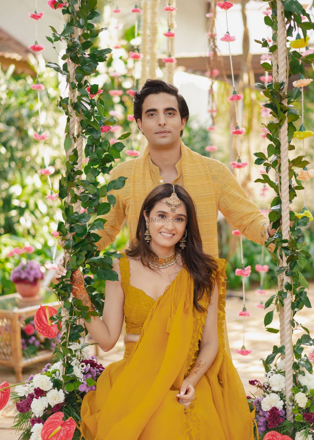 Photo of Colour coordinated couple sitting on a floral swing in matching ochre yellow outfits