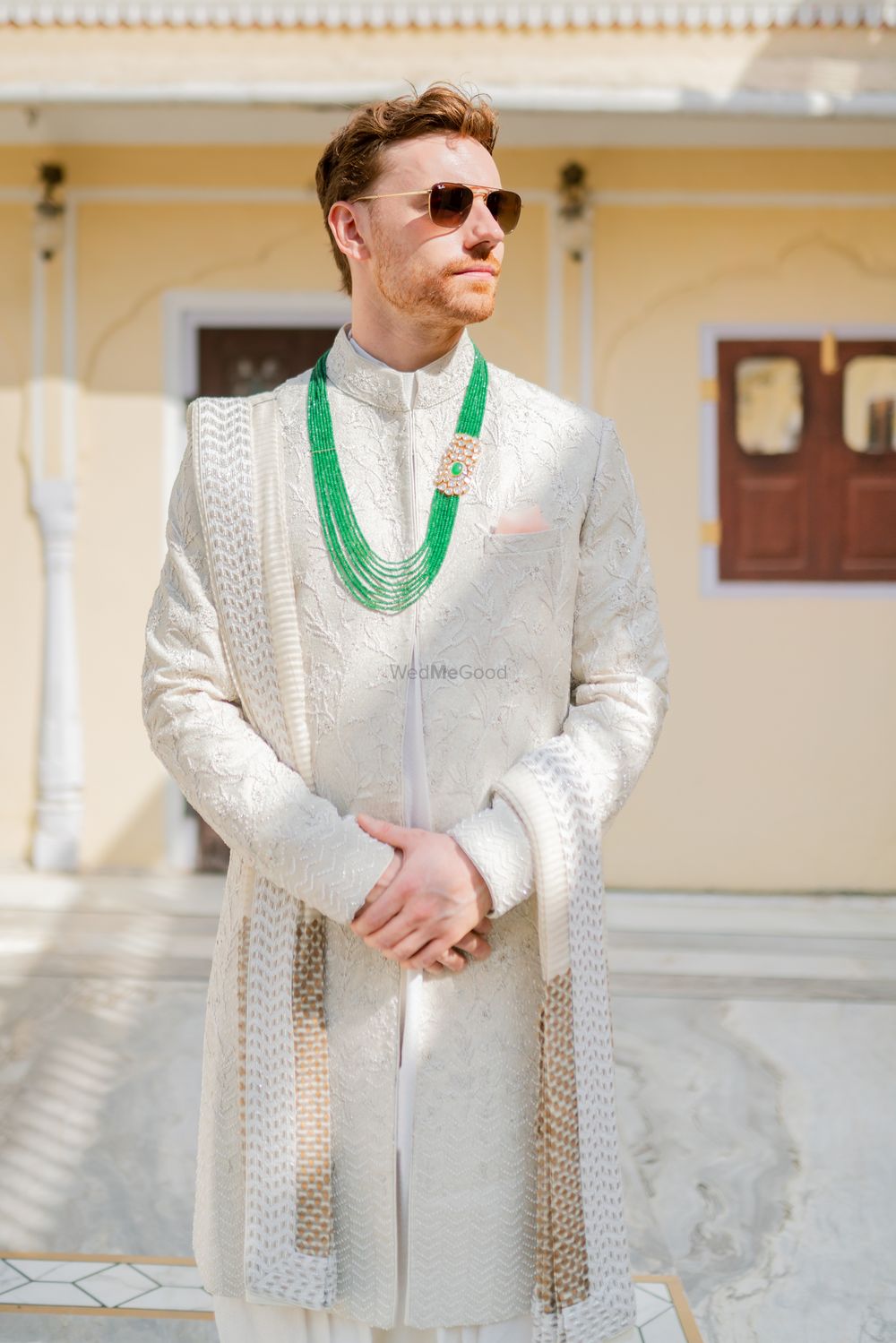 Photo of groom in ivory sherwani with green jewellery
