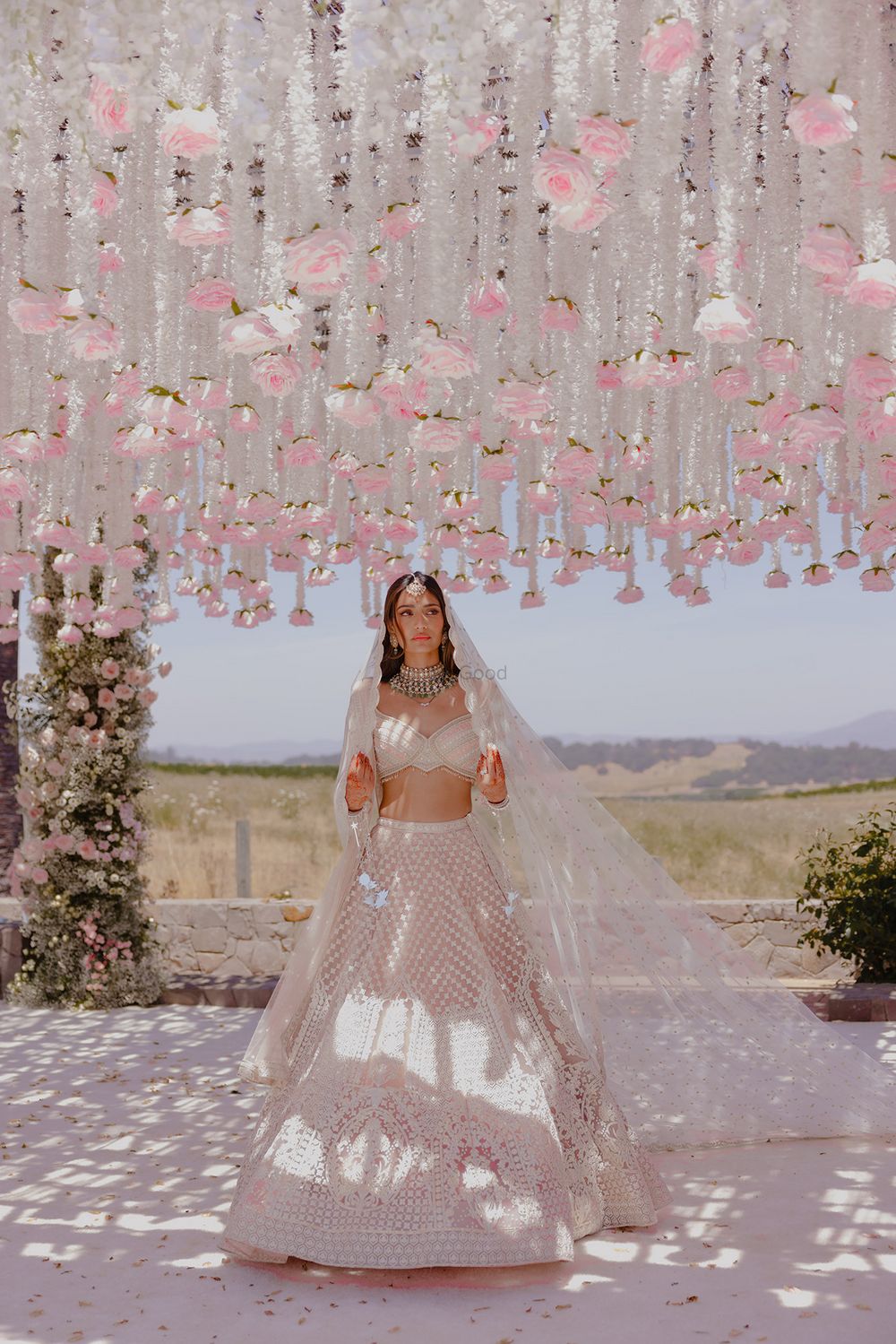 Photo of Stunning bridal portrait with bride in a pastel lehenga and hanging floral decor elements in white and baby pink