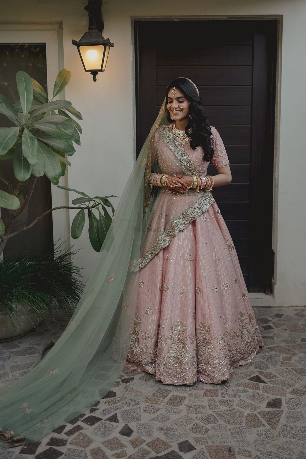 Photo of bride in pretty pastel pink lehenga with blue veil