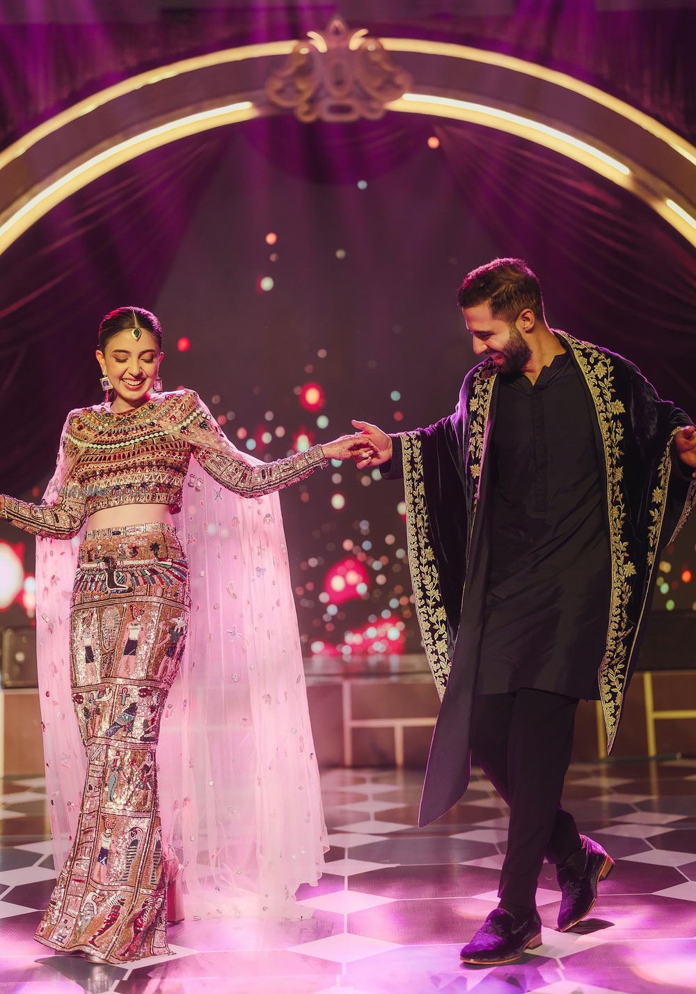 Photo of dancing couple on stage for sangeet with bride in a cape lehenga