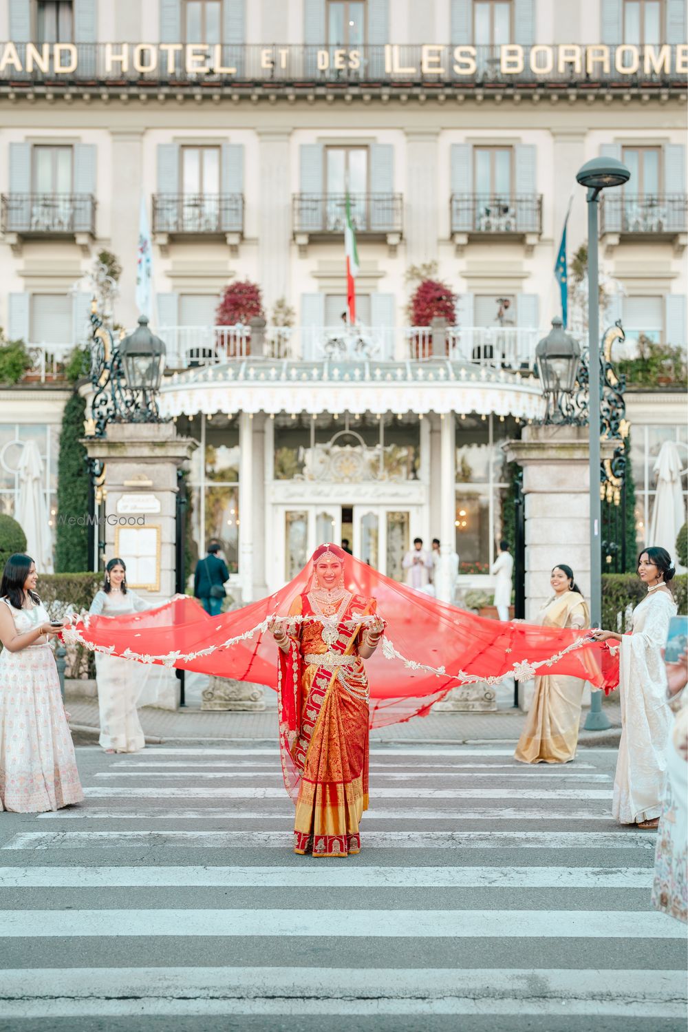 Photo of Grand bridal entry in a red saree and her bridesmaids holding the veil on the wedding day