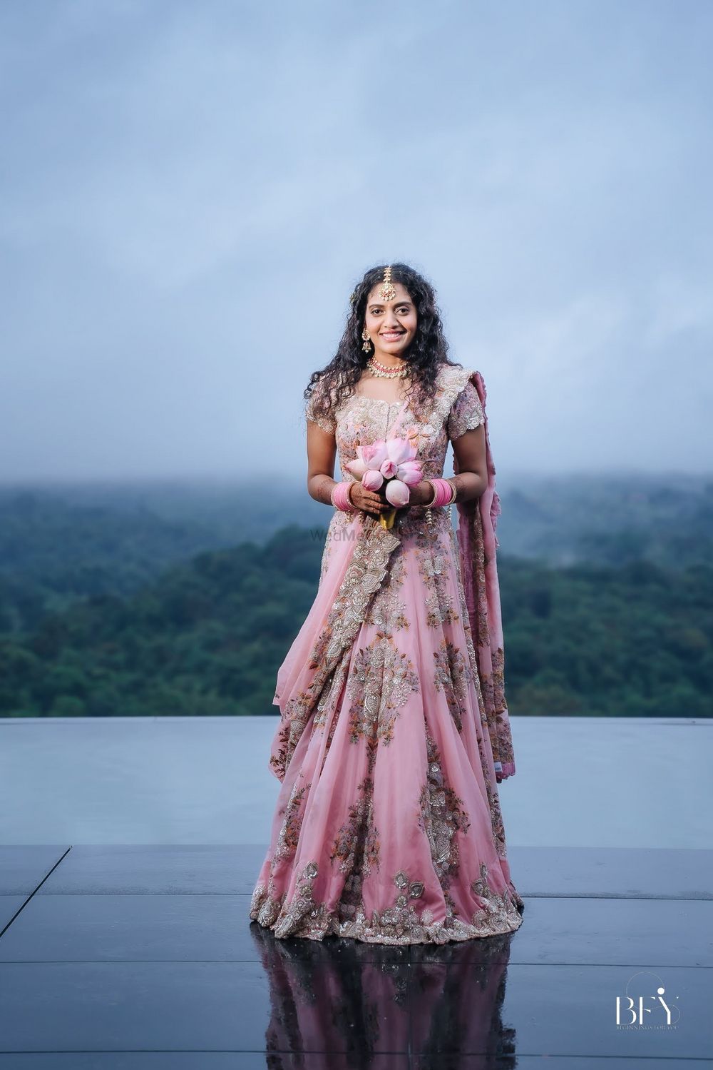 Photo of pink and gold bridal lehenga with bouquet of lotus