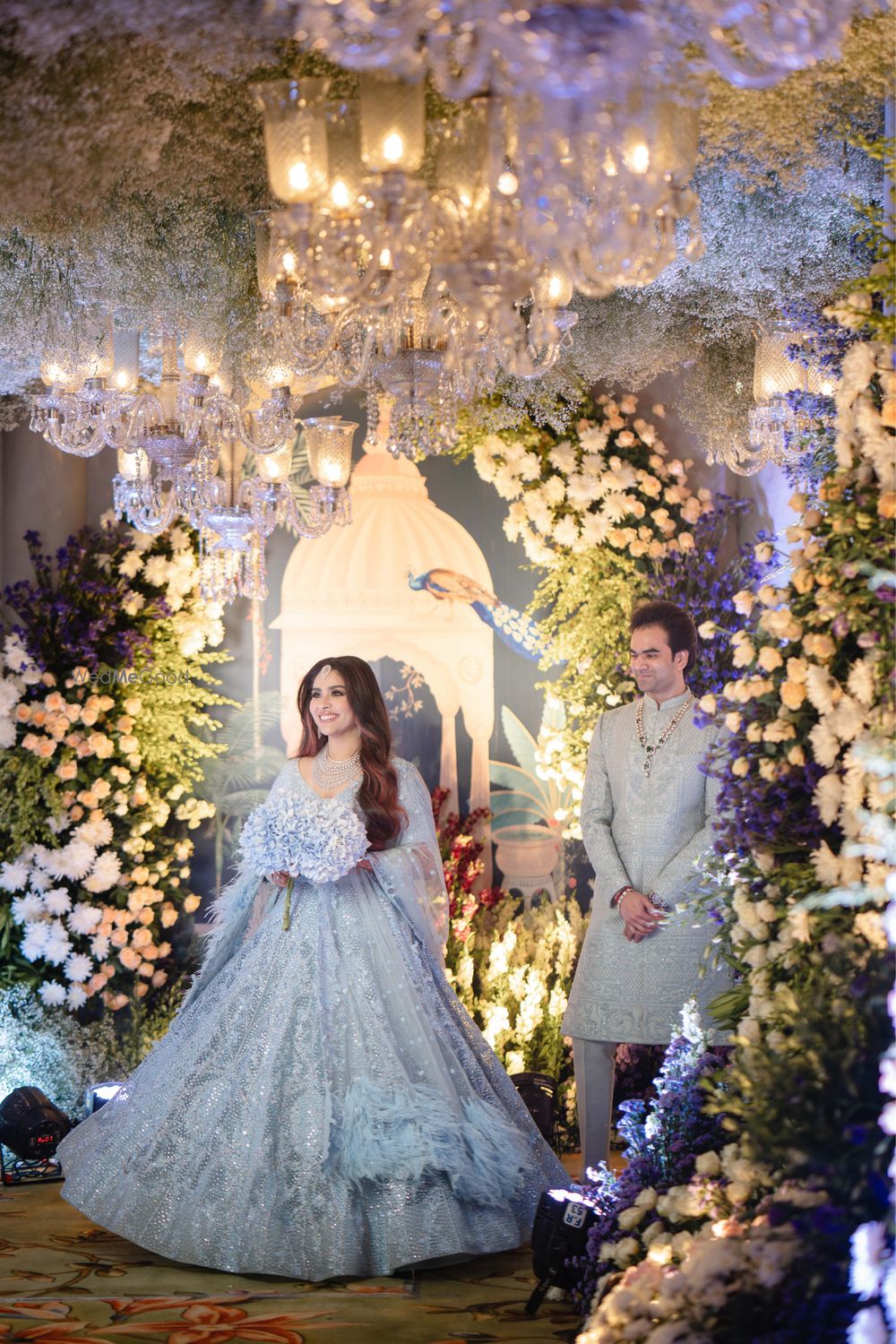 Photo of Lovely couple shot with the bride in a powder blue lehenga and the groom in a matching outfit with stunning floral decor