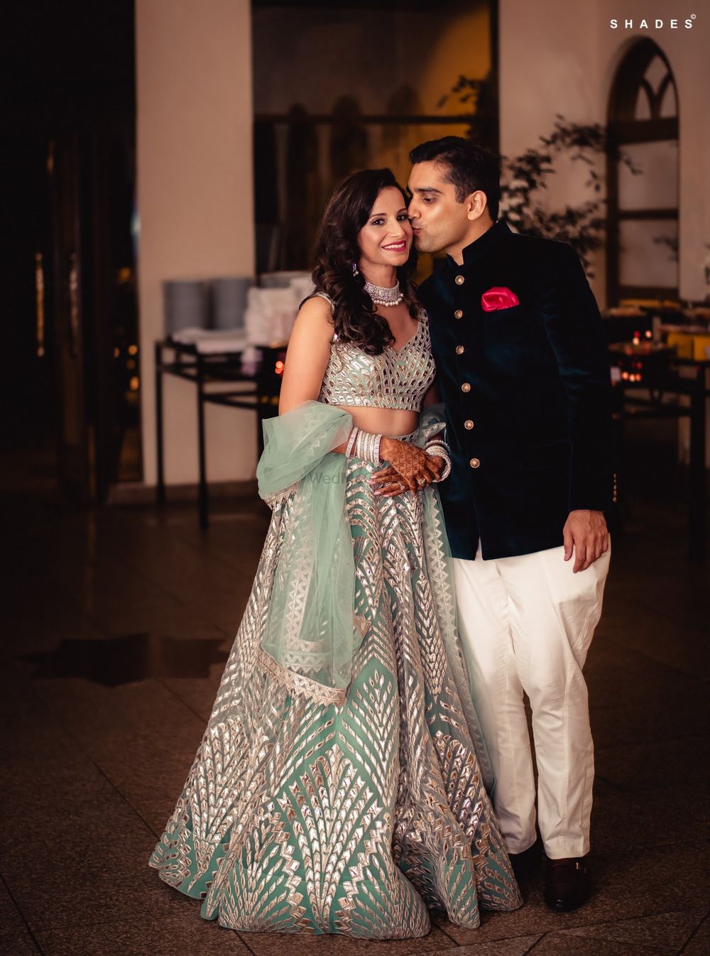 Photo of A bride in a shimmer lehenga posing with her groom-to-be at their sangeet