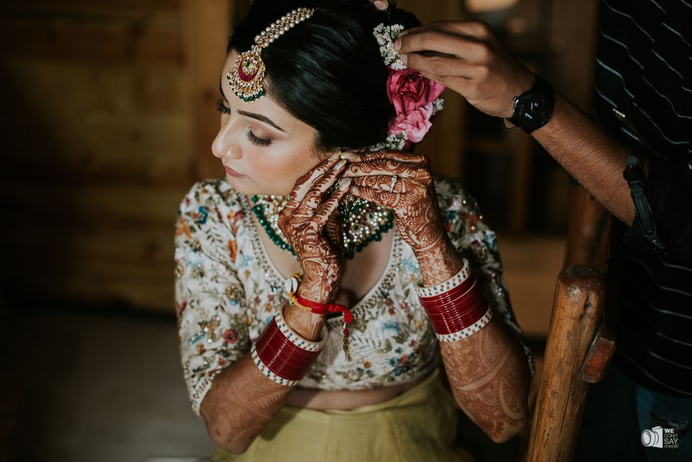 Photo of A bride gets ready to put on her jewelry while getting her bun adorned with roses.