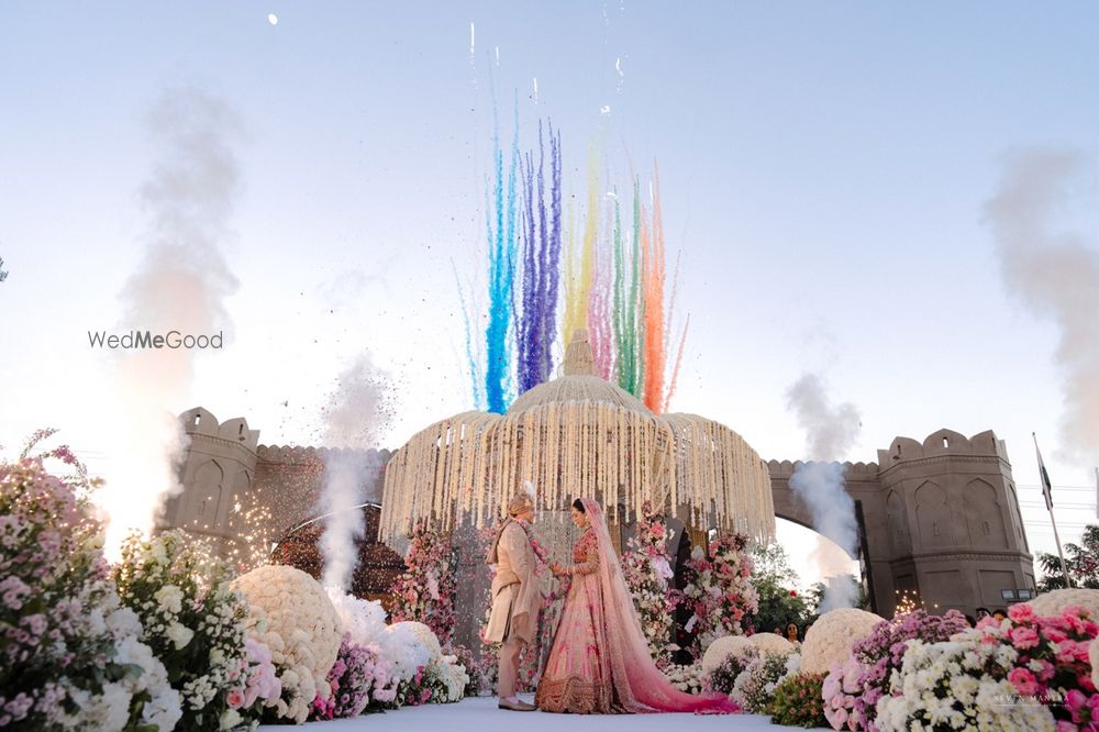 Photo of Lovely shot of the bride and groom against pastel decor and smoke bomb style fireworks going off