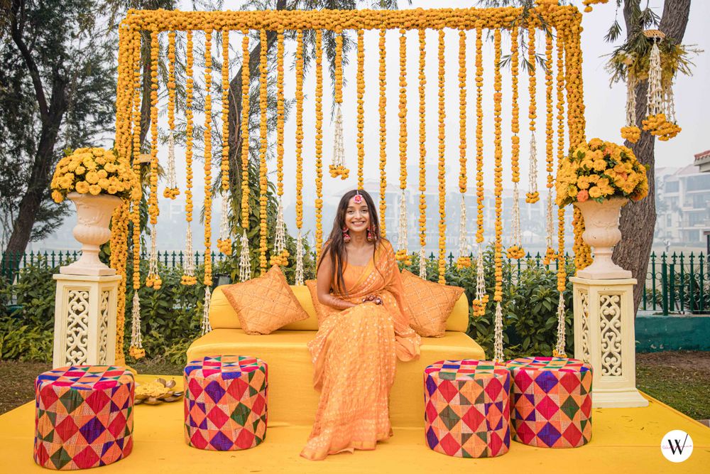 Photo of bride in yellow saree against pretty haldi backdrop