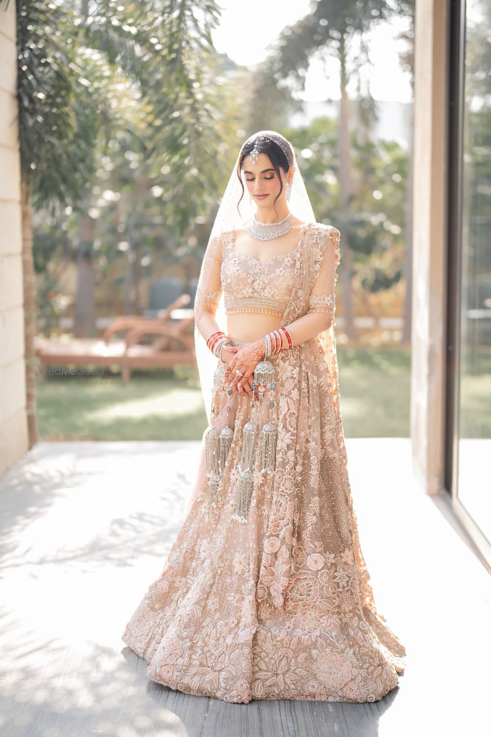 Photo of Bride in a gorgeous pastel peach lehenga in lace with diamond jewellery and matching kaleeras