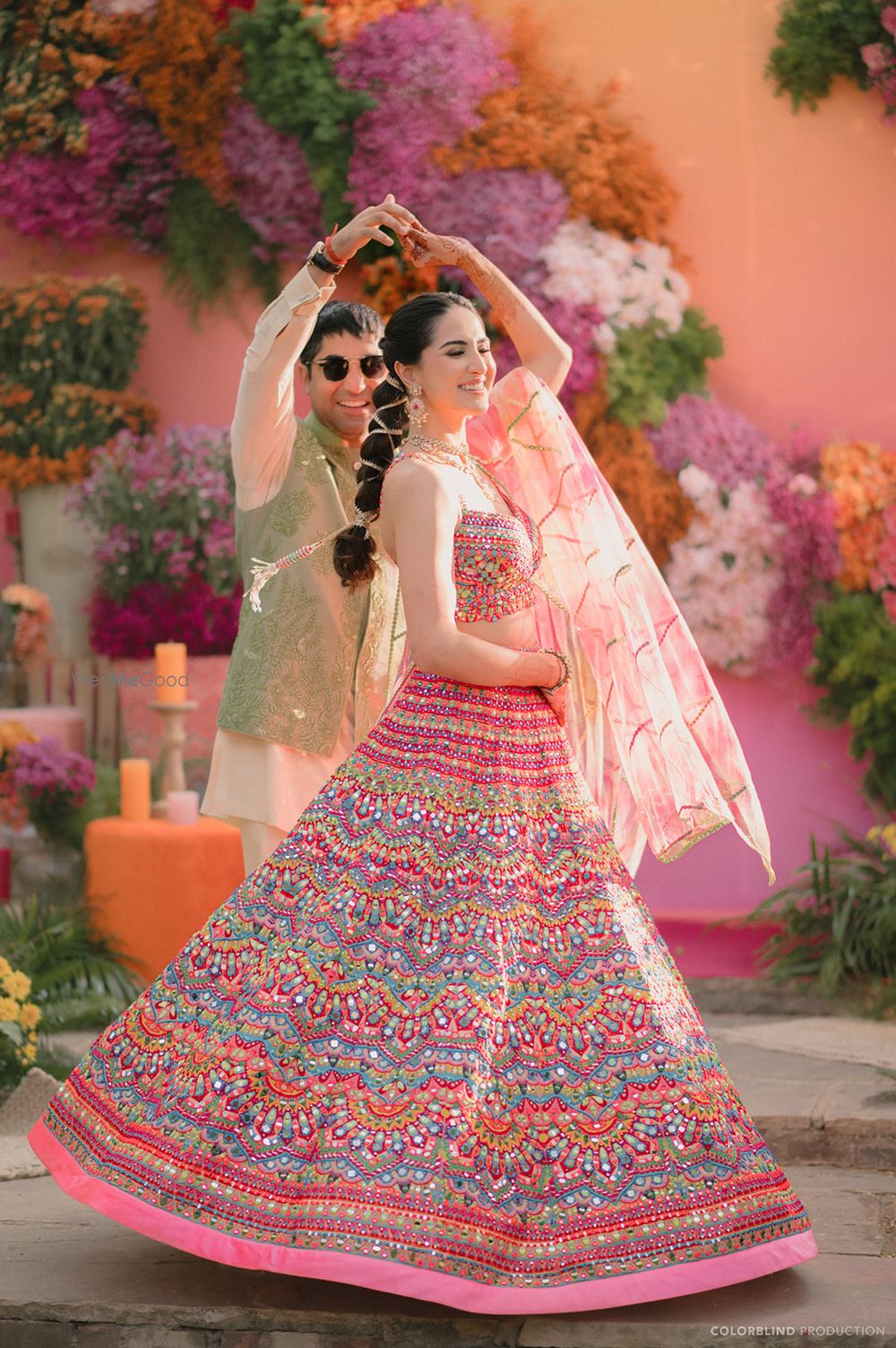 Photo of Groom twirls the bride on the mehendi event and the bride wears a lovely colourful lehenga and braid look