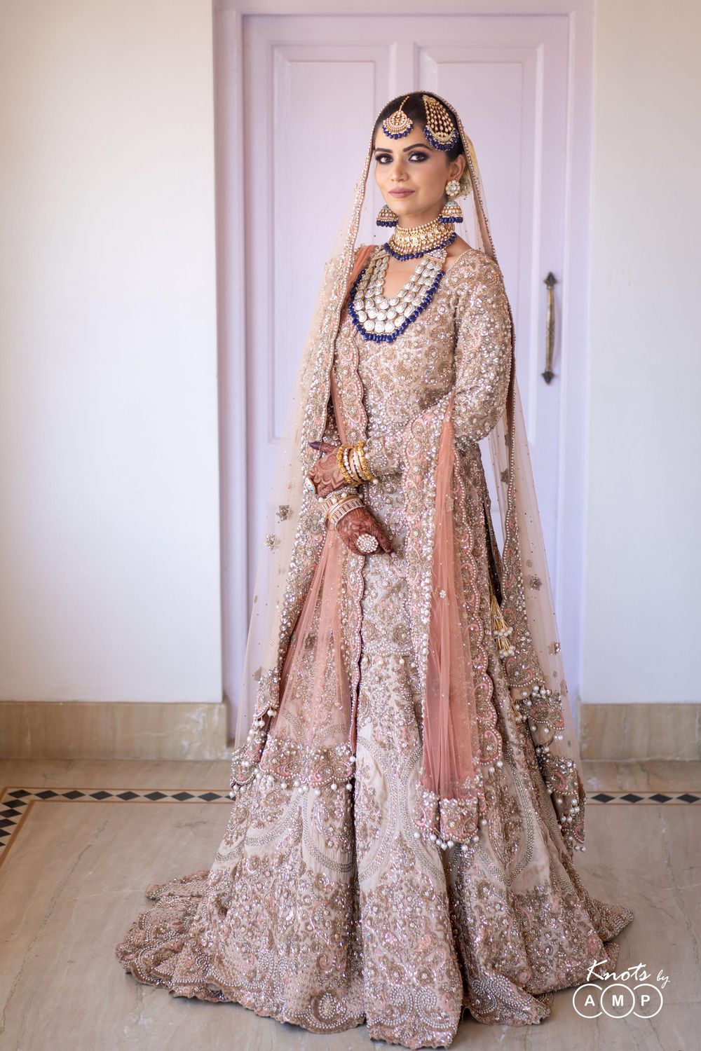 Photo of A beautiful bride in peach bridal heavy sharara and exquisite jewellery with dark blue beads.