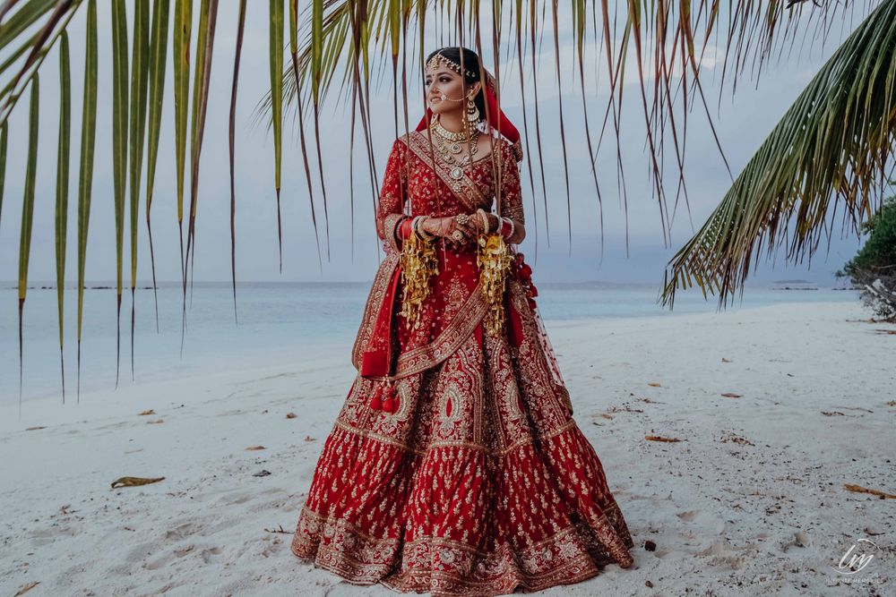 Photo of beach wedding with the bride posing in her deep red lehenga