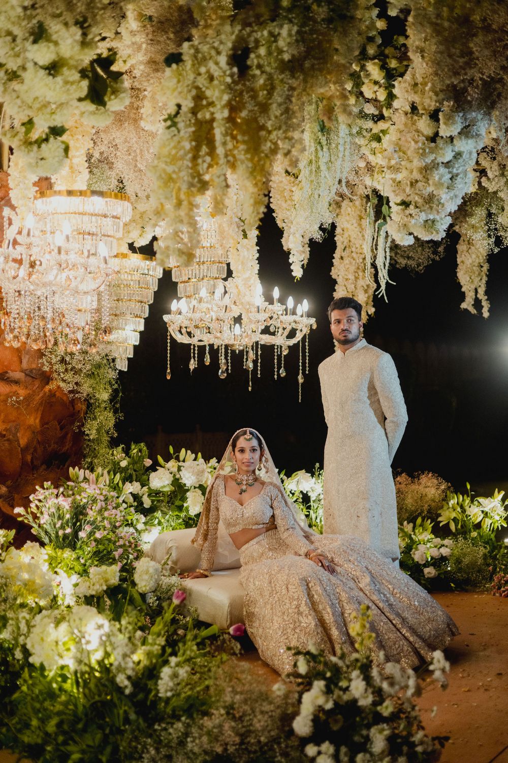 Photo of Stunning couple portrait on the all-white mandap, laden with white florals and chandeliers.