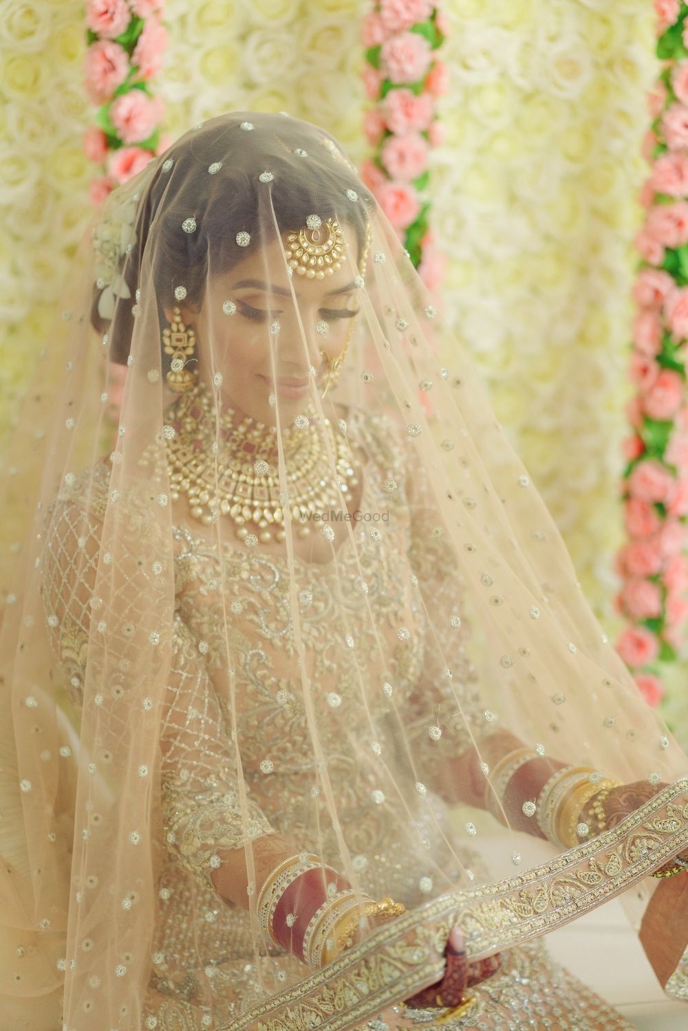 Photo of Bride in light peach lehenga holding dupatta as veil