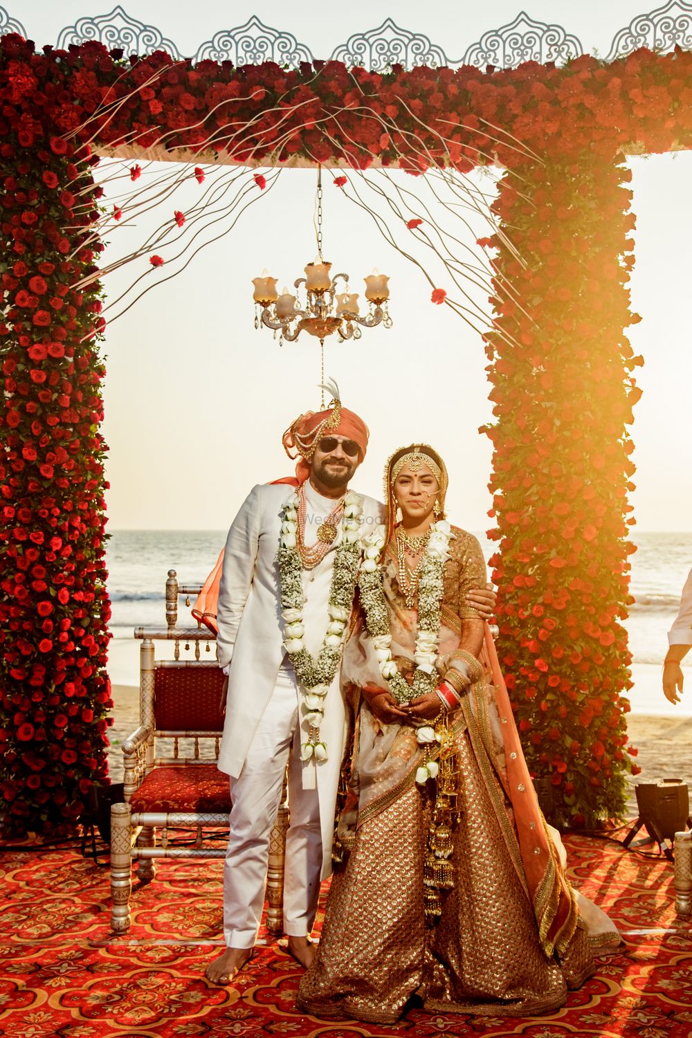 Photo of matching bride and groom with orange and white outfits and beachside mandap