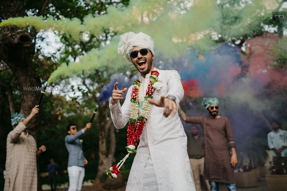 Photo of Fun groom shot with groom dancing and smoke bombs in the background