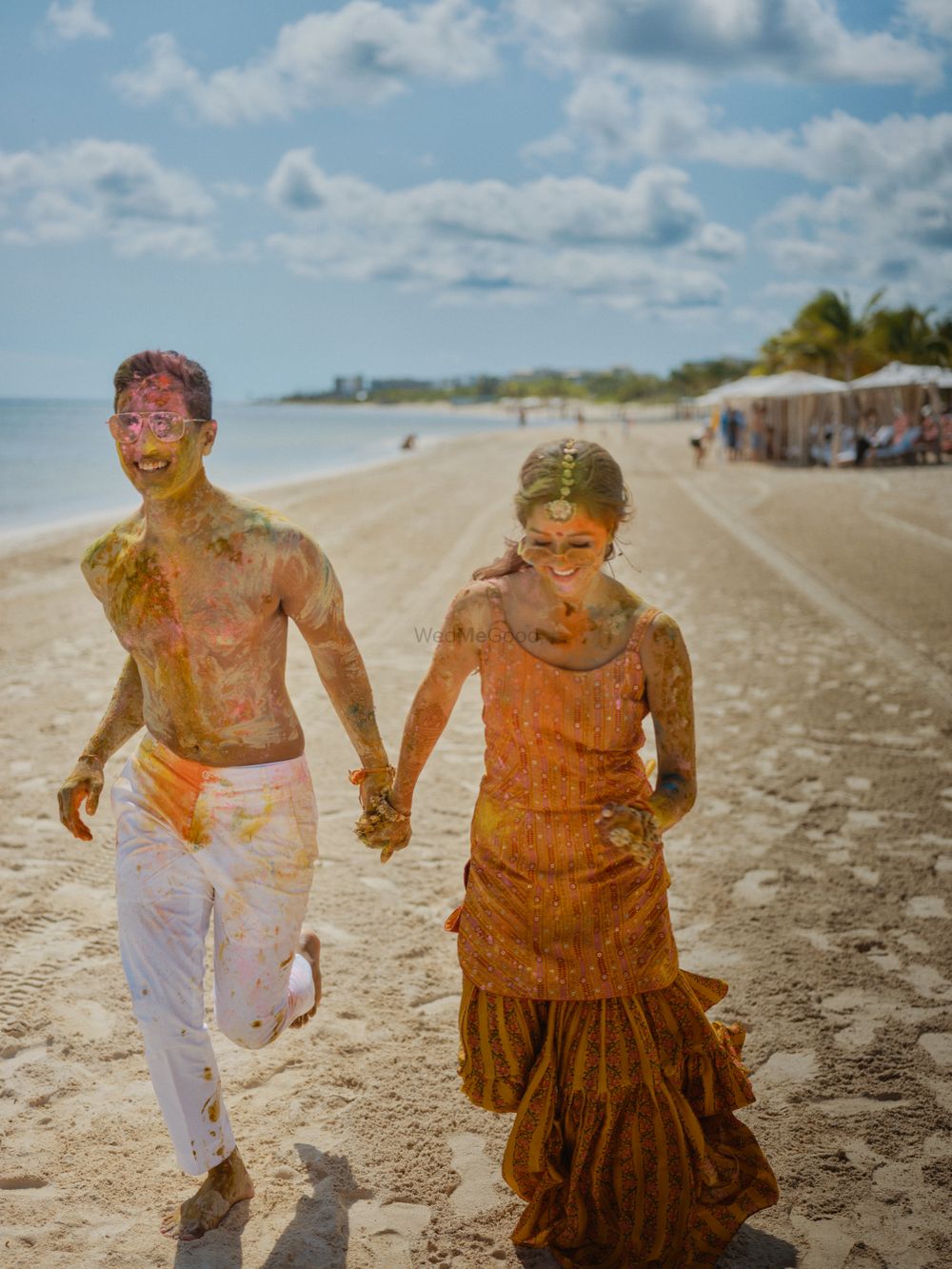 Photo of fun haldi shot with bride and groom running on the beach
