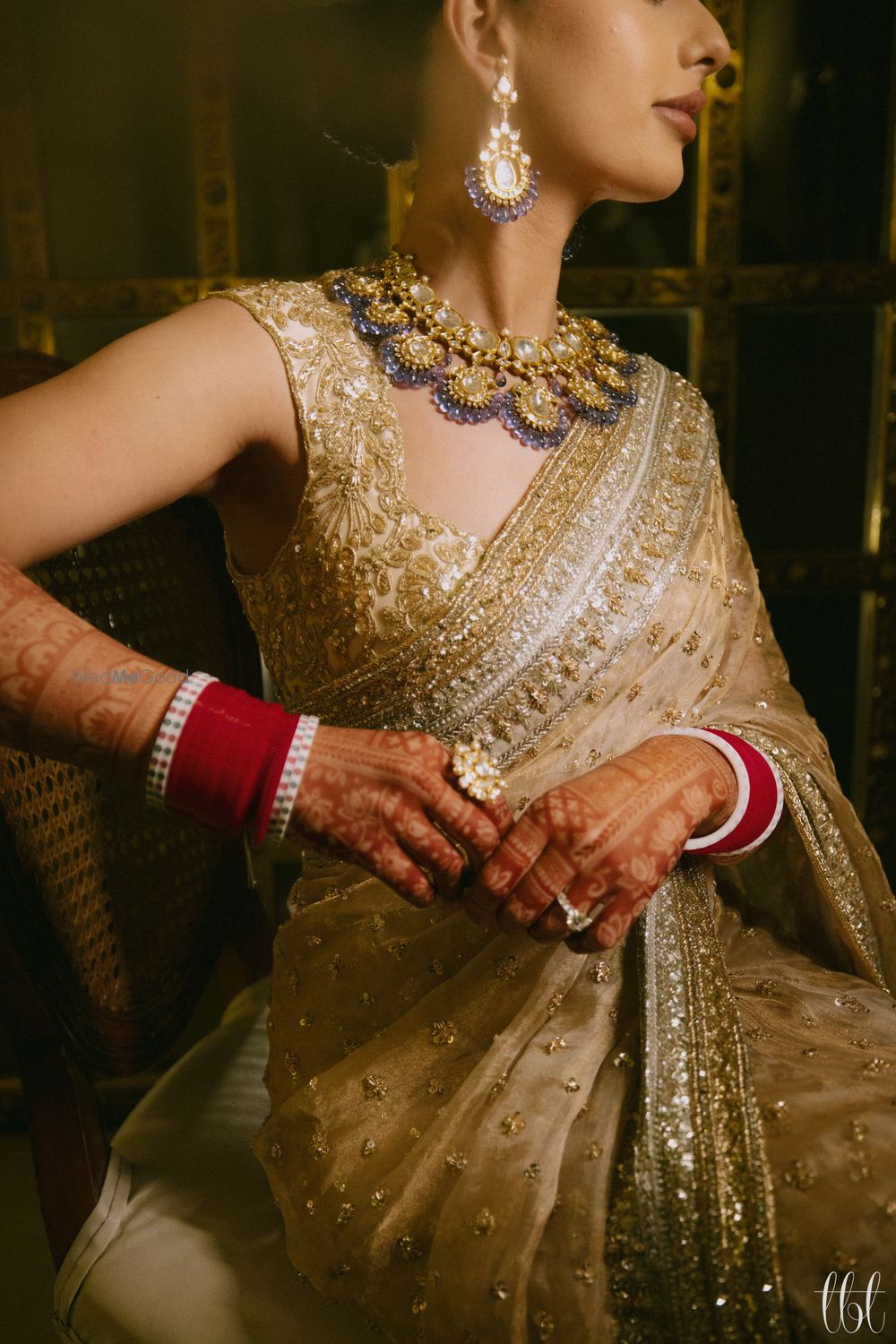 Photo of Gorgeous shot of the bride wearing a statement bib style necklace with lavender detailing, statement rings and a red chura to compliment her gold saree look.