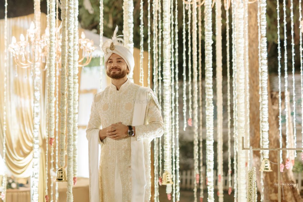 Photo of groom in traditional cream sherwani with gold embroidery against floral decoration