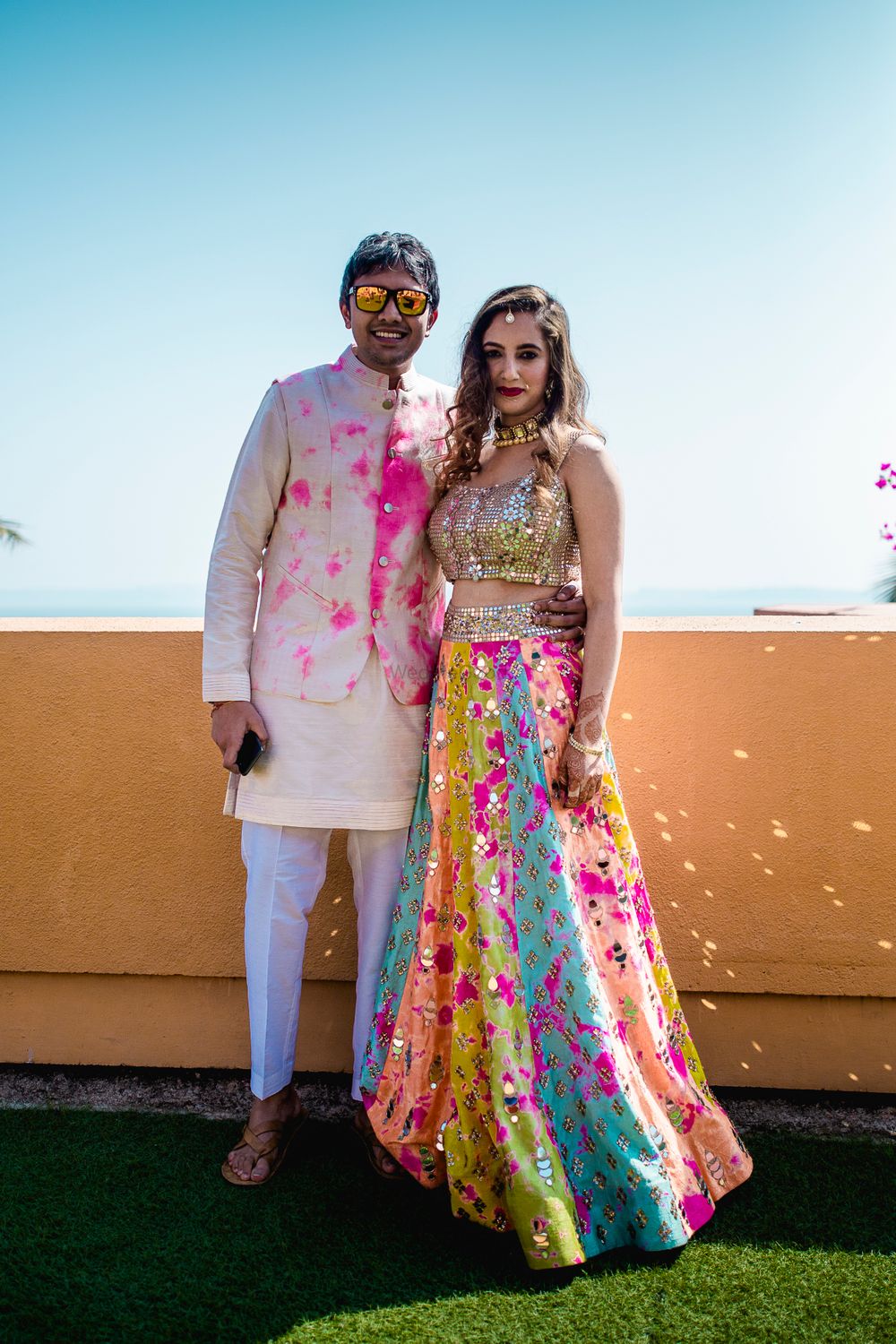 Photo of Bride and groom coordinating in tie and dye outfits on their Mehndi.