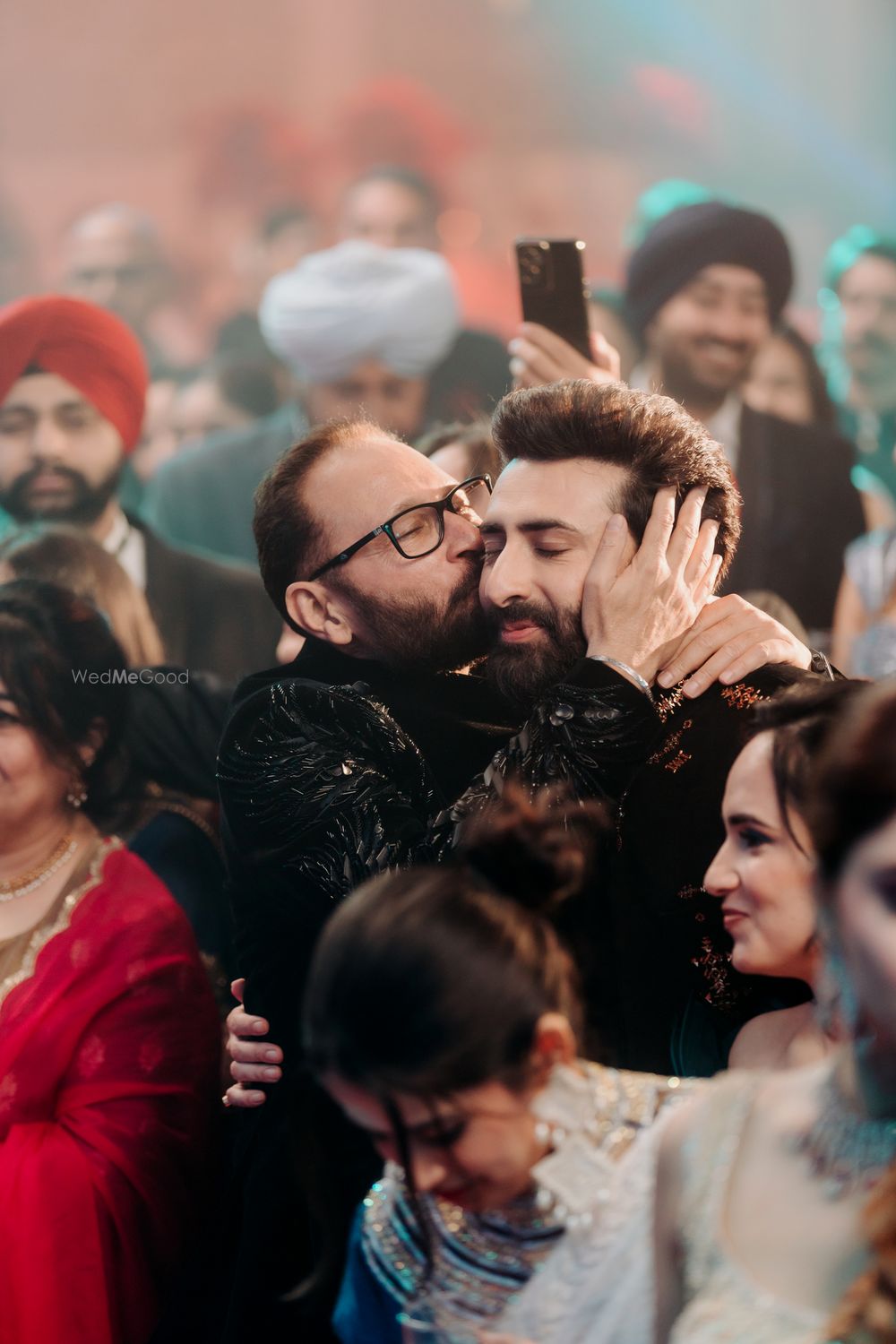 Photo of A candid shot of the father of the groom kissing the groom on the sangeet day