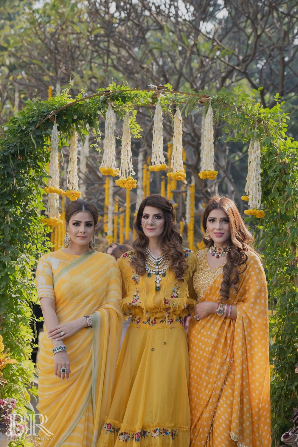 Photo of bride and her sisters in matching yellow outfits on mehendi