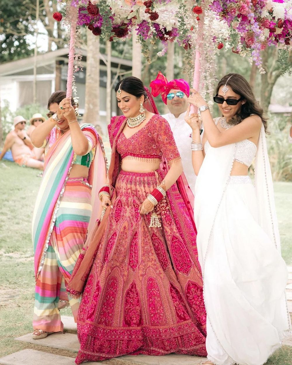 Photo of Bride in red and pink lehenga entering with her mom and sisters