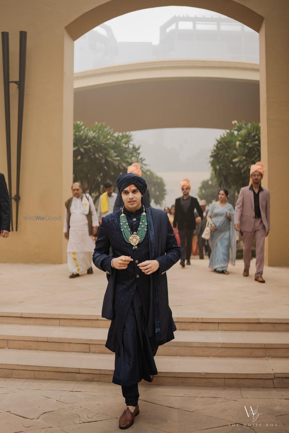 Photo of Groom entering the wedding venue in an all-black sherwani and jade green statement jewellery
