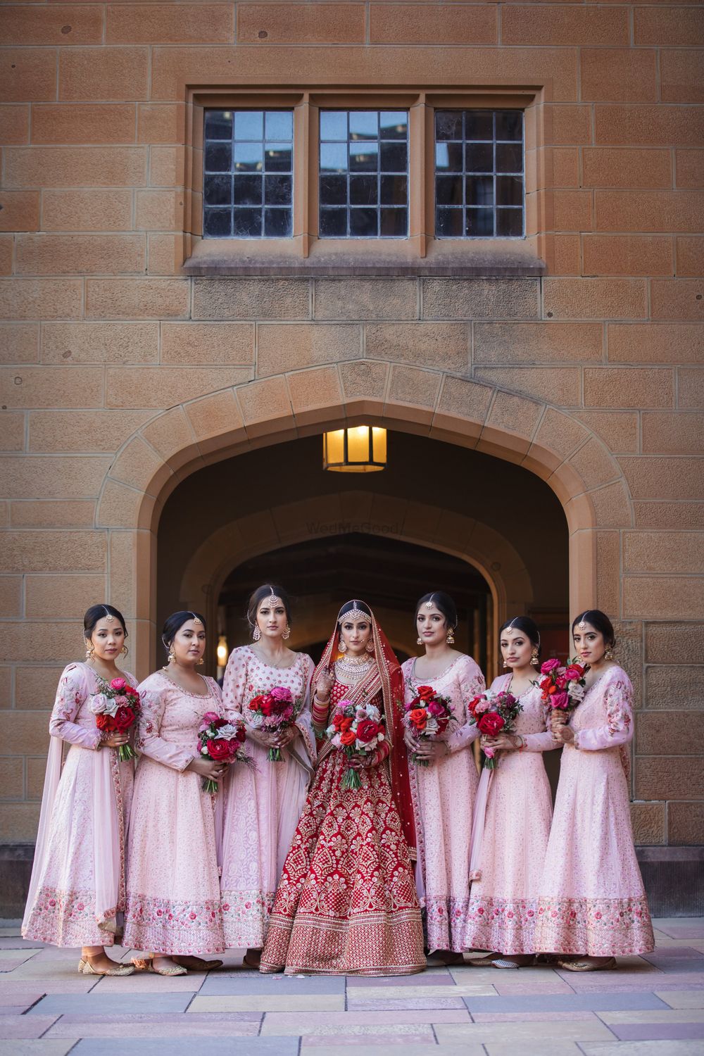 Photo of A bride in red with bridesmaids in light pink