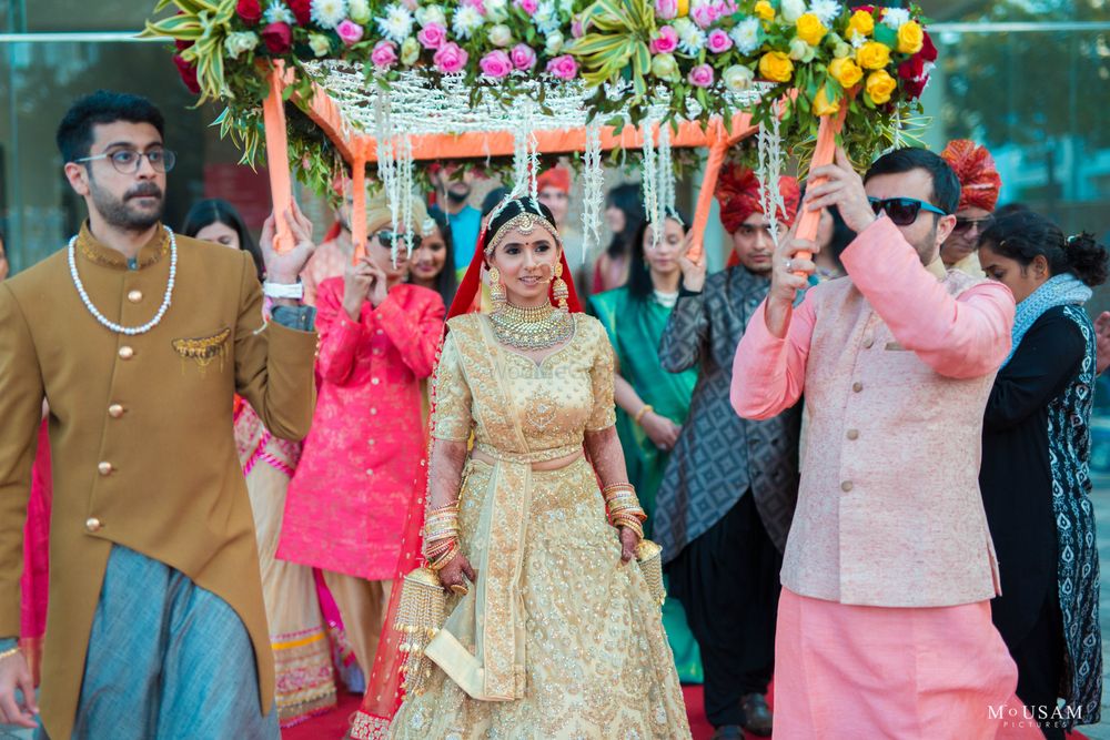 Photo of bride in gold lehenga entering under phoolon ka chadar