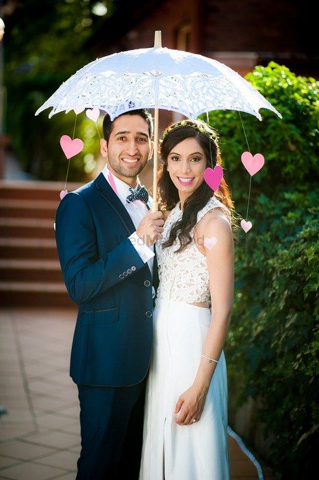 Photo of pre wedding shoot with lace umbrella and hanging pink paper hearts swishing through the wind