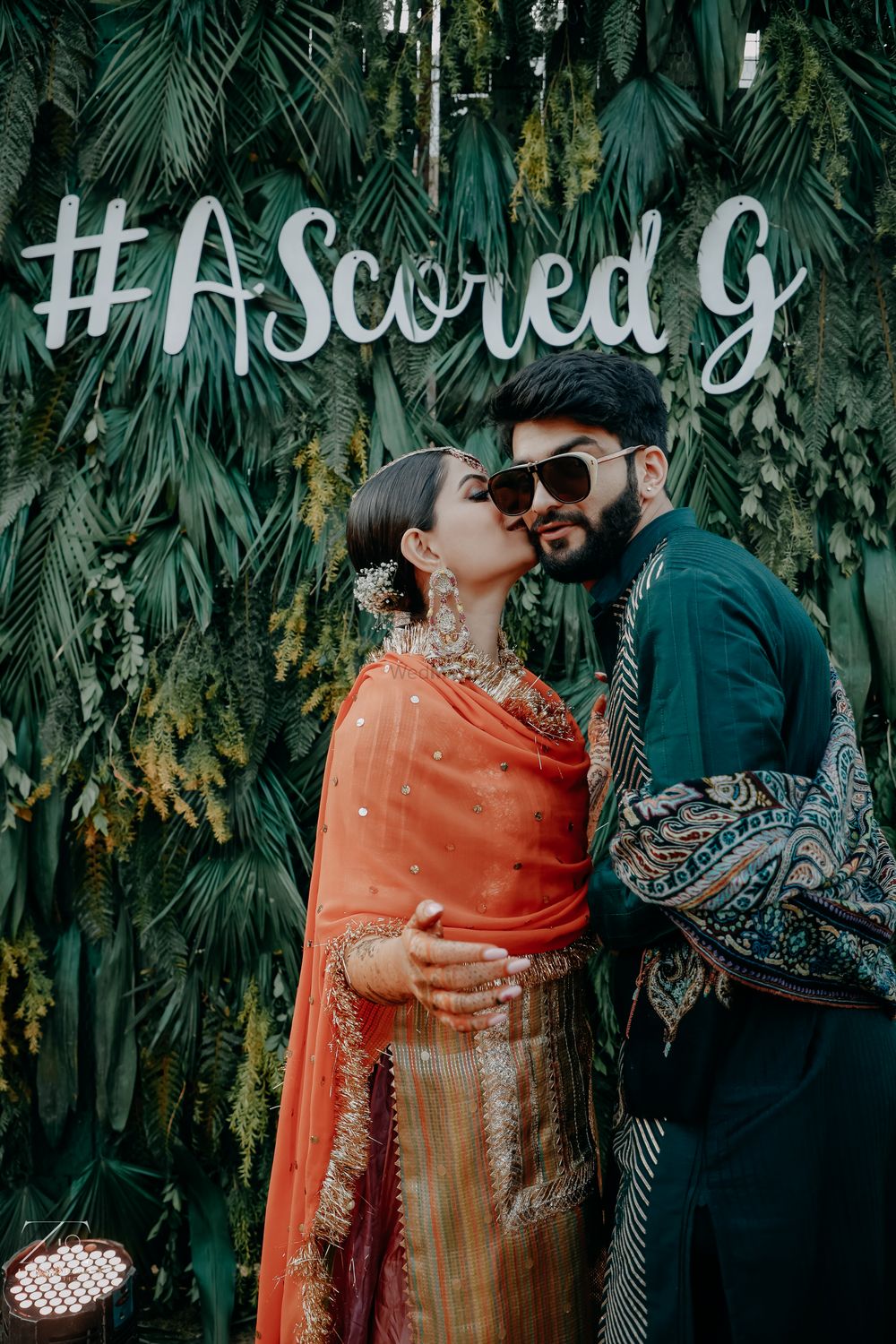 Photo of bride kissing groom in front of their wedding hashtag