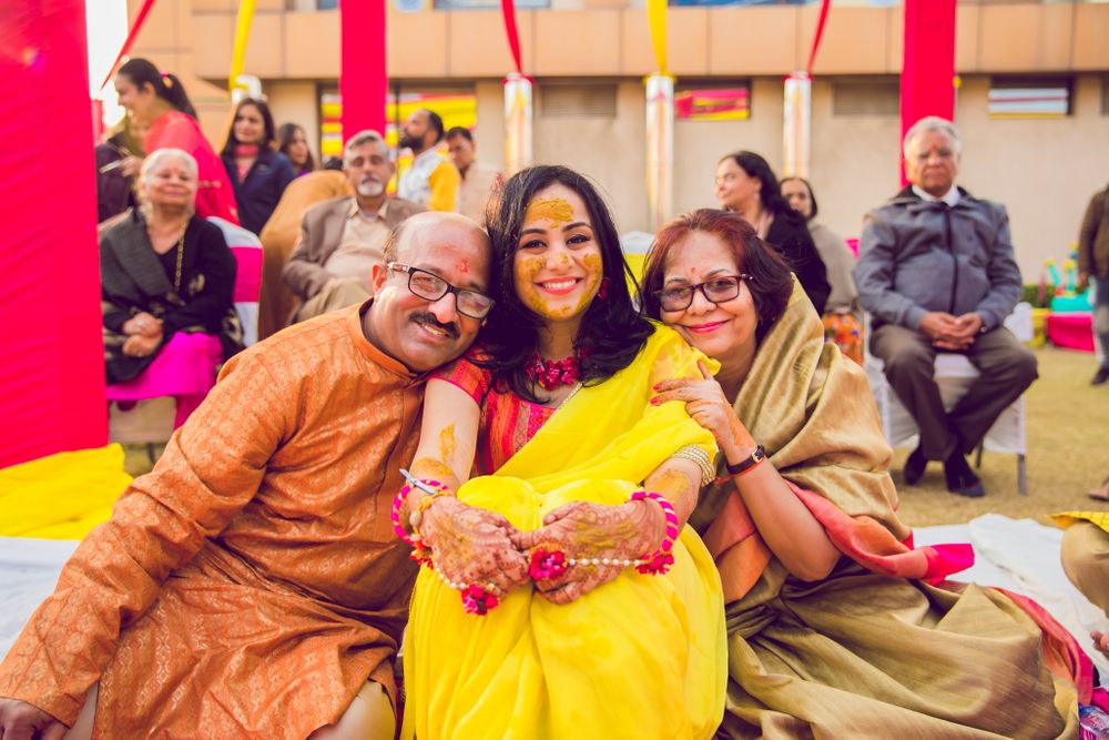 Photo of A cute photograph of a bride with her parents on haldi.
