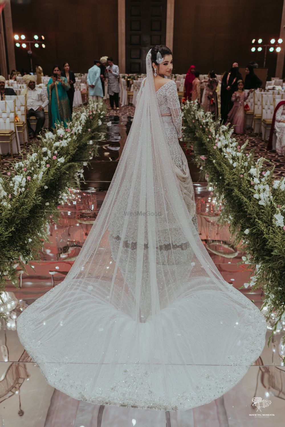 Photo of bride entering her wedding in a white bridal lehenga with a train