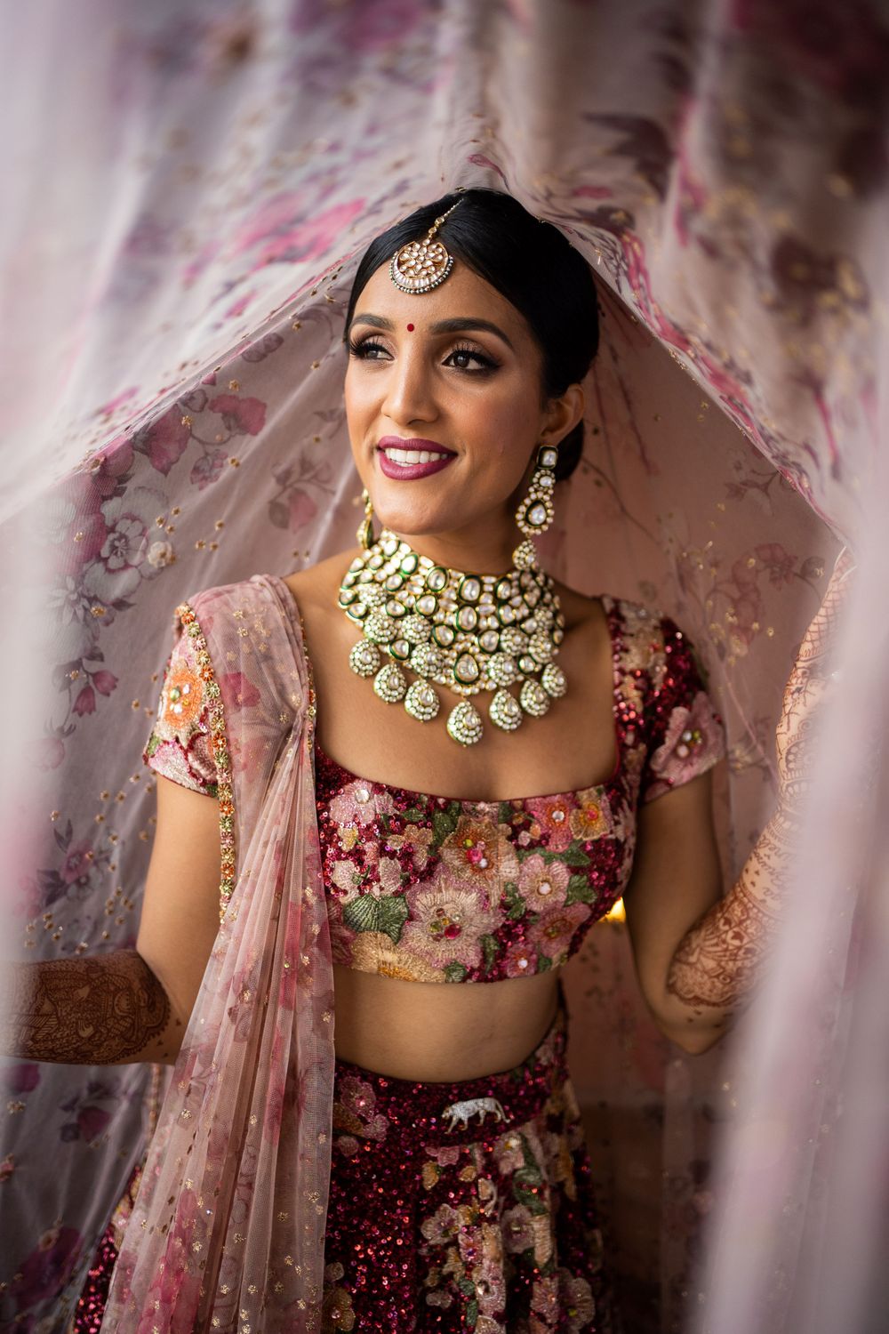 Photo of bride in marsala floral lehenga and contrasting polki jewellery with printed dupatta