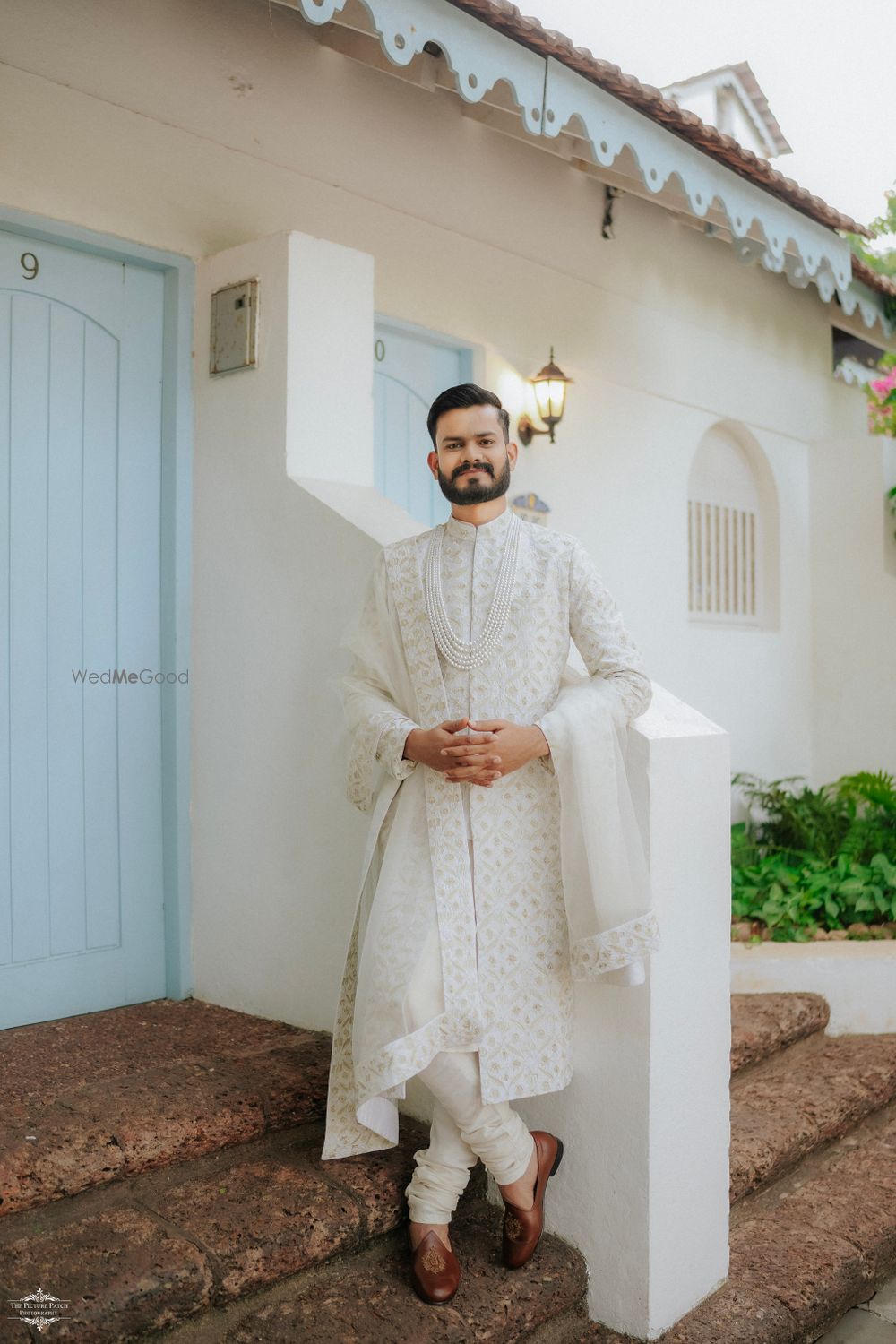 Photo of A monotone all-white sherwani with matching pearls and contrast juttis for the groom on the wedding day