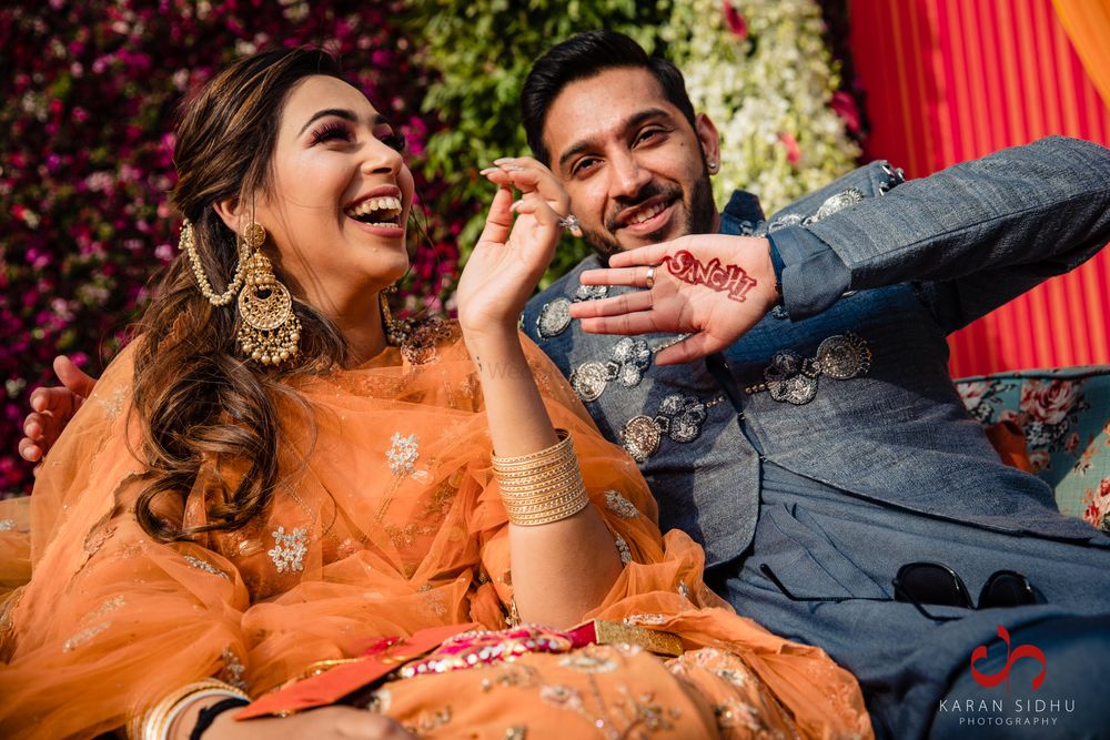 Photo of happy couple shot with groom showing off his mehendi