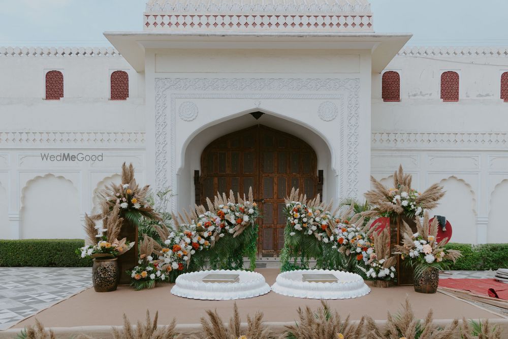 Photo of Outdoor haldi setup with fresh and dry floral arrangements and white urlis