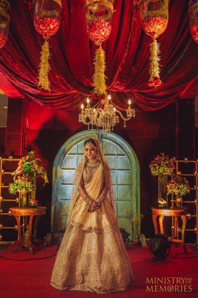 Photo of Bride posing in gold lehenga with red decor